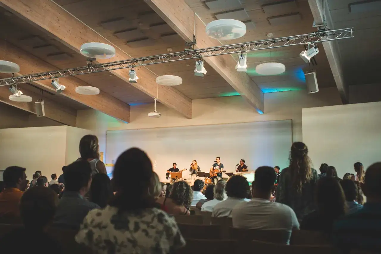 Menschen lauschen einer Band auf einer B&uuml;hne in einem modernen Gotteshaus. Die Architektur erinnert an eine erf sekte.