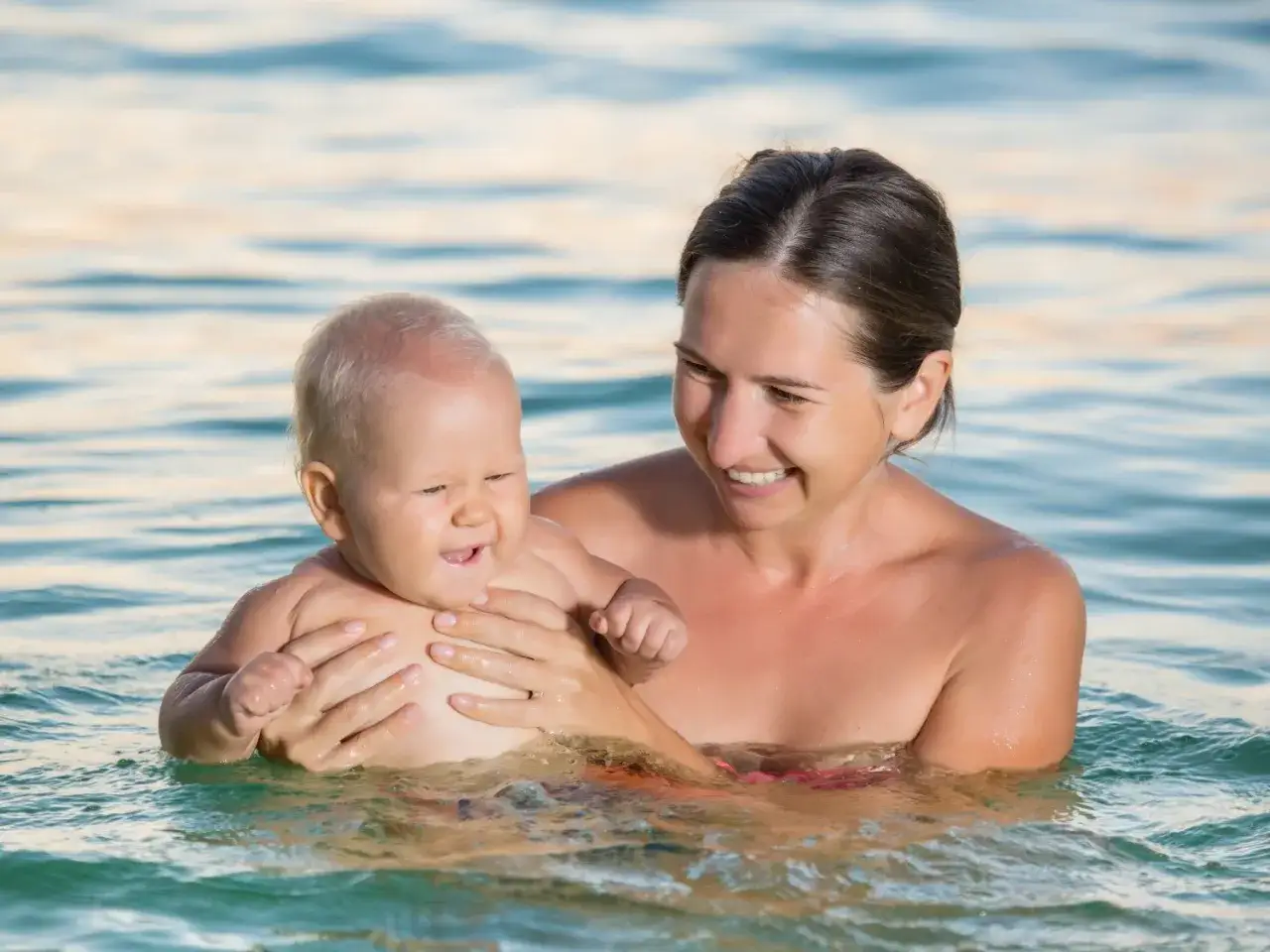 Glad mamma h&aring;ller sitt barn i vattnet, en h&auml;rlig stund f&ouml;r babysim oavsett &aring;lder.