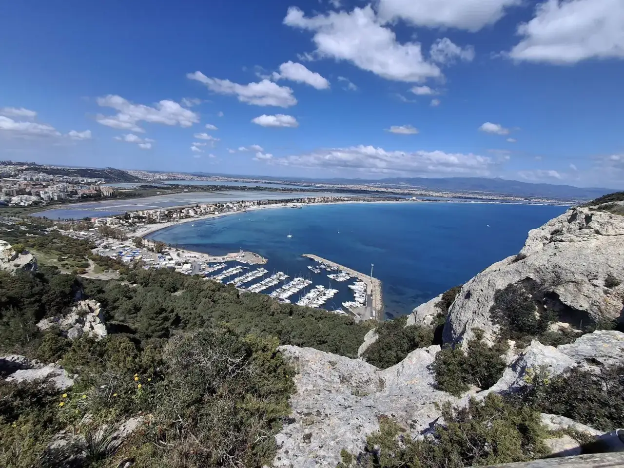 Widok na zatokę z łodziami i miastem w tle. Piękne plaże Cagliari kuszą błękitem wody.