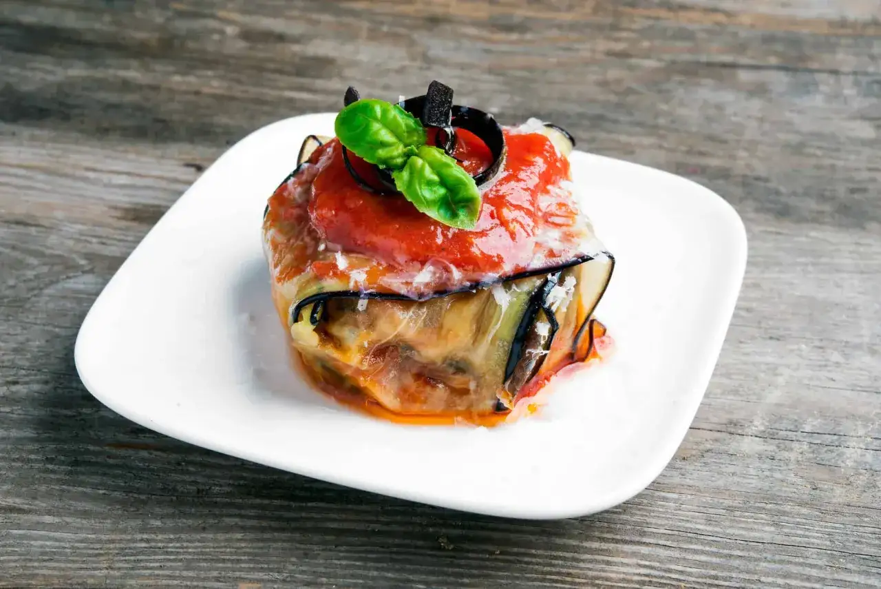 Ein köstlicher Auberginenauflauf italienisch, geschichtet mit Tomatensoße, Käse und frischem Basilikum, serviert auf einem weißen Teller.