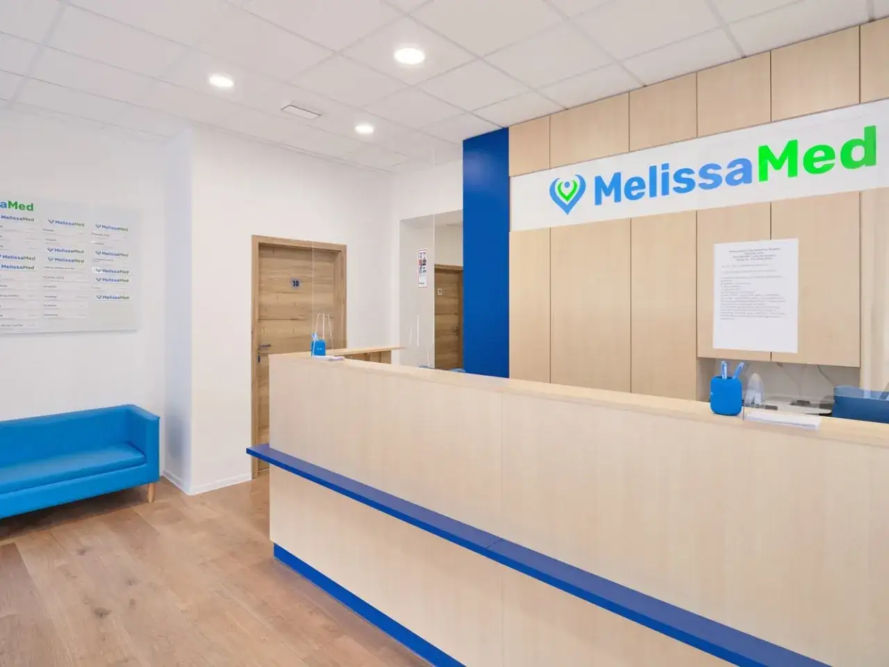 Recepcja nowoczesnej kliniki medycznej MelissaMed z niebieską kanapą i drewnianymi elementami.