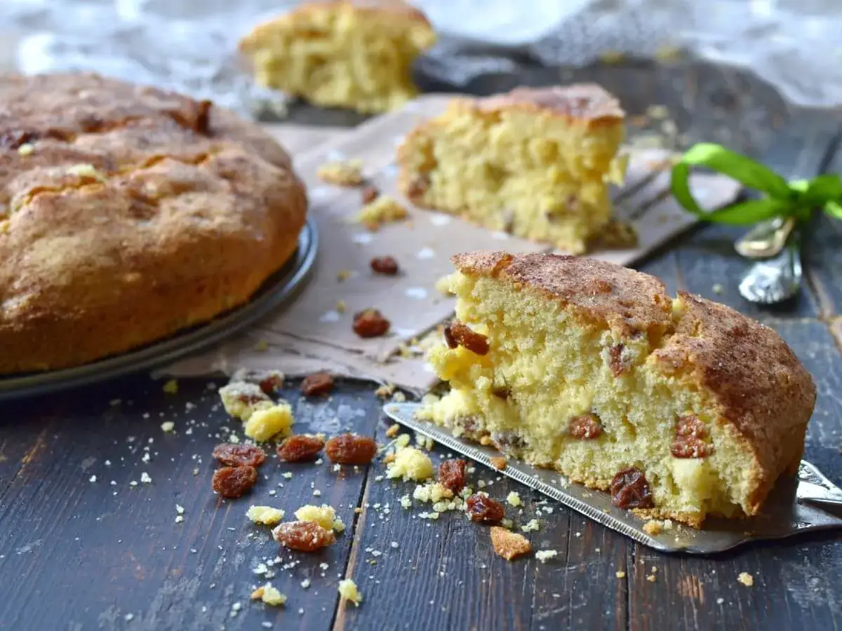 Una fetta di torta senza zucchero, soffice e dorata, con uvetta e una spolverata di cannella. Perfetta per una colazione sana.