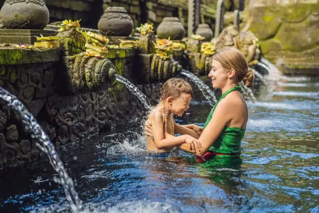 Madre e hijo disfrutan de un ba&ntilde;o refrescante en una fuente sagrada en Asia. El ni&ntilde;o r&iacute;e mientras el agua le salpica.
