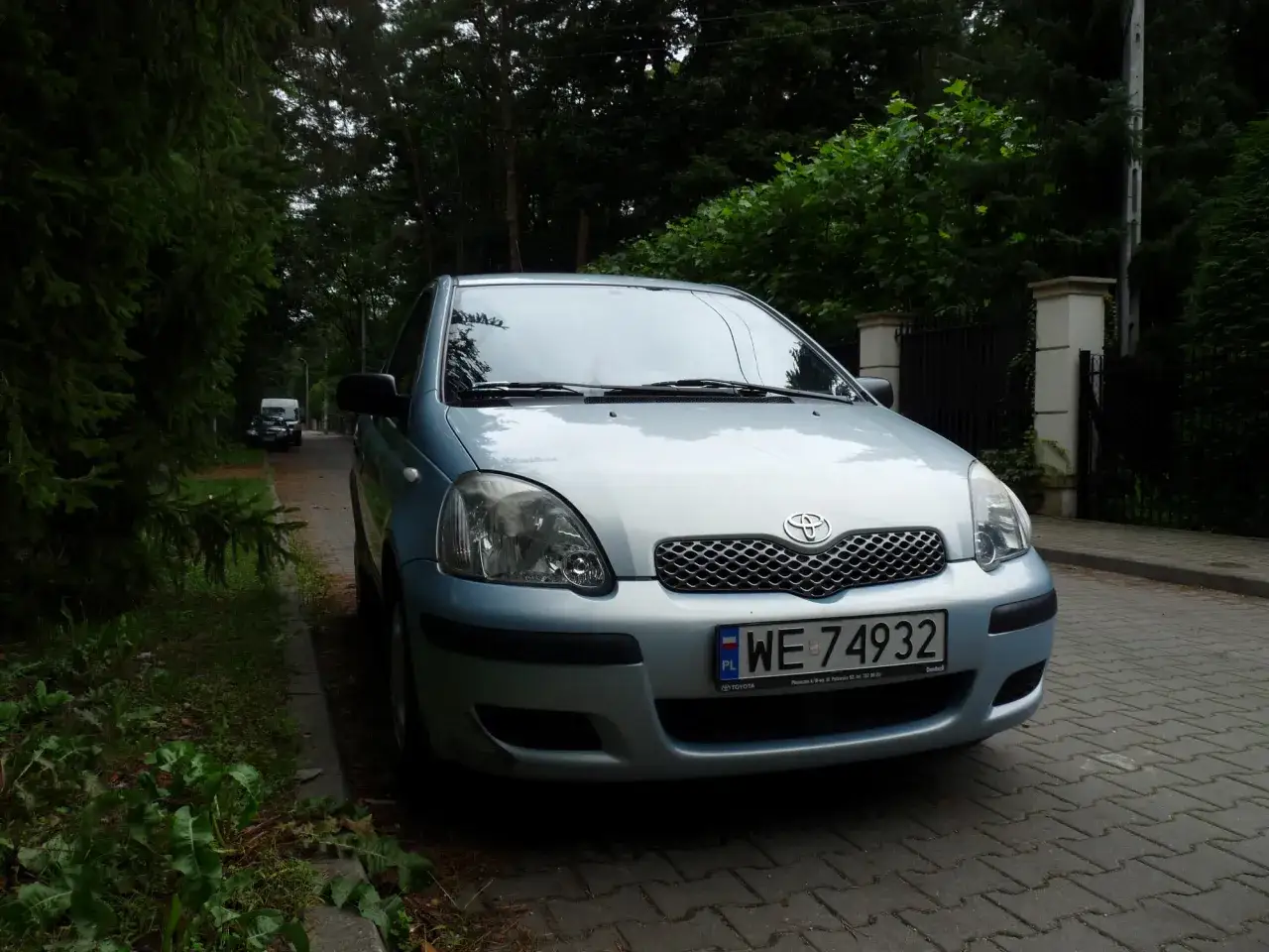 Jasnoniebieski model Toyoty na 5 liter, zaparkowany przy zalesionej ulicy.
