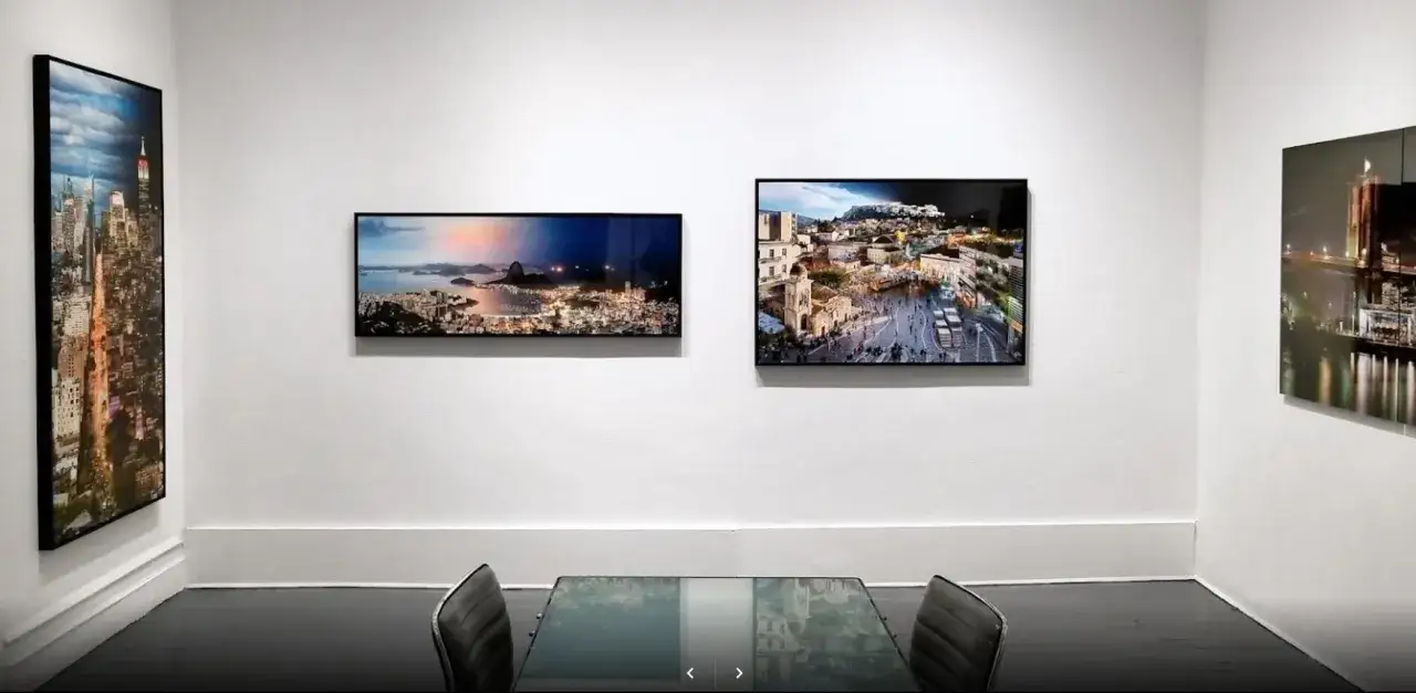 A gallery wall showcases cityscapes: New York, Rio de Janeiro, and Athens. A glass table with chairs sits in the foreground, reflecting the art, a true photo eye.