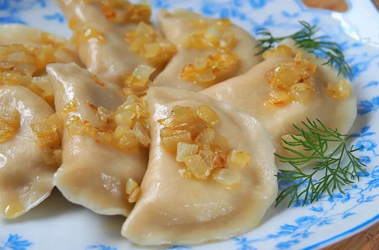 Pyszne pierogi ruskie z podsmażoną cebulką i koperkiem na talerzu z niebieskimi wzorami.