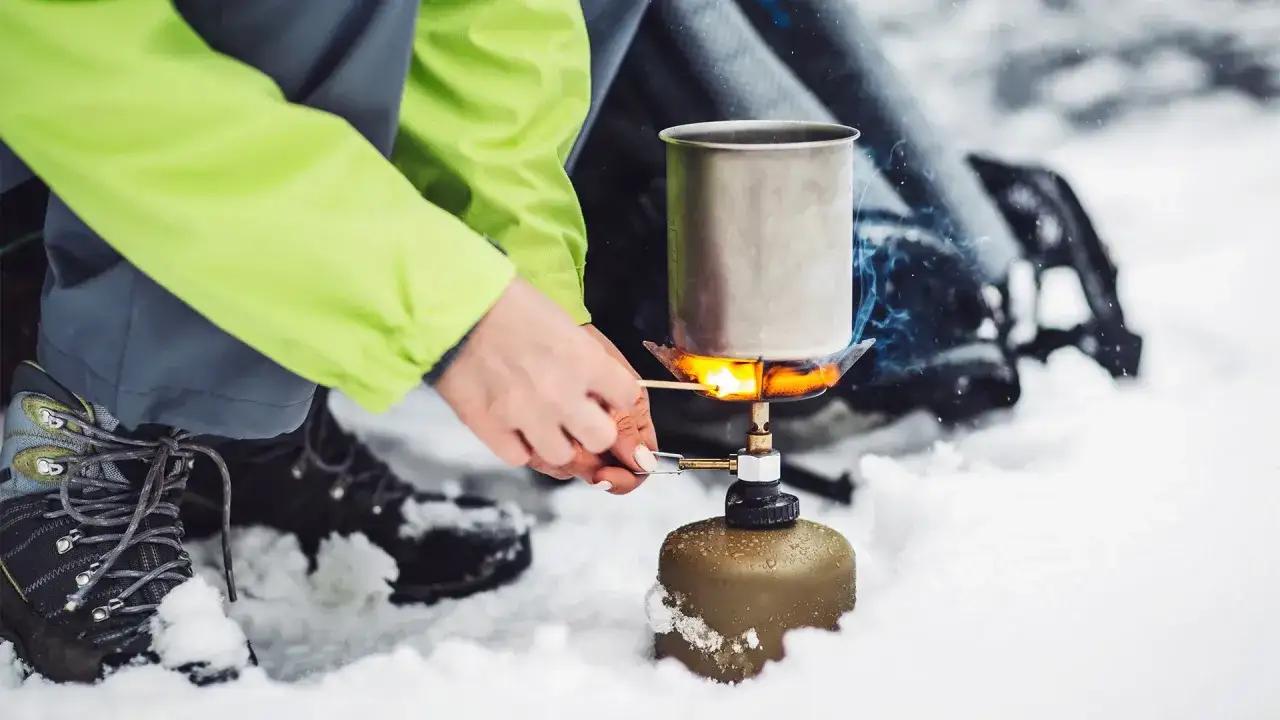 Tändning av ett bensinkök i snön. En person i en ljusgrön jacka tänder en eld med en tändsticka.