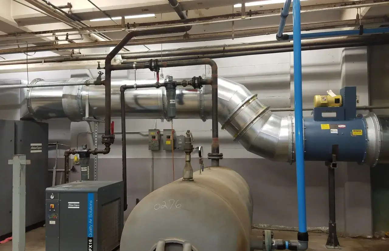 Sistema de tuberías industriales con un gran tanque de aire y un motor de compresor de aire azul con un motor amarillo en la parte superior.