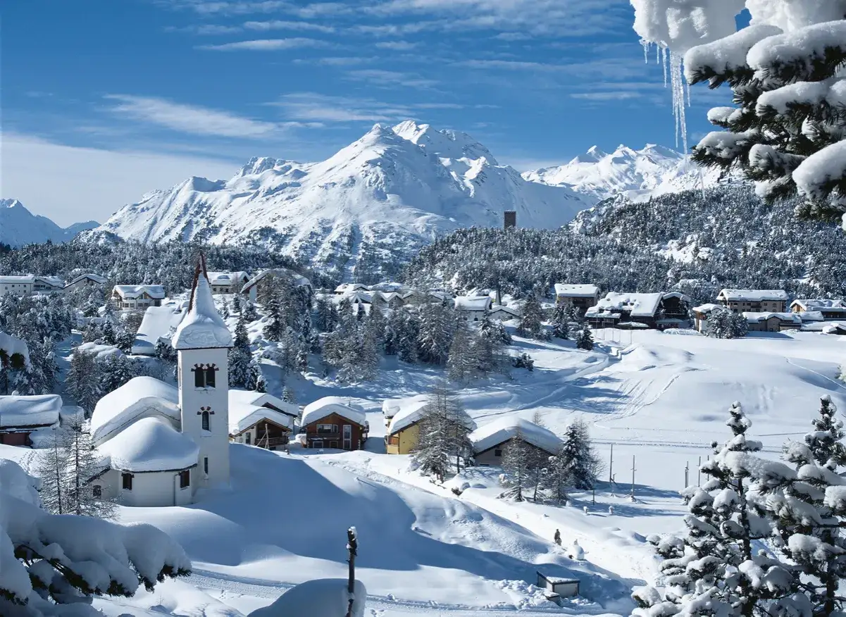 Winterliche Idylle in der Schweiz: Ein verschneites Dorf mit Kirche und Bergen im Hintergrund.