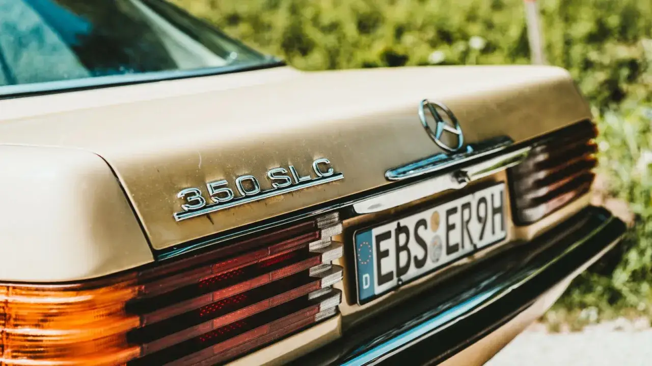 Detalle de un Mercedes 350 SLC dorado, con su matrícula lista para la ITV. La luz de la matrícula se ve nítida.