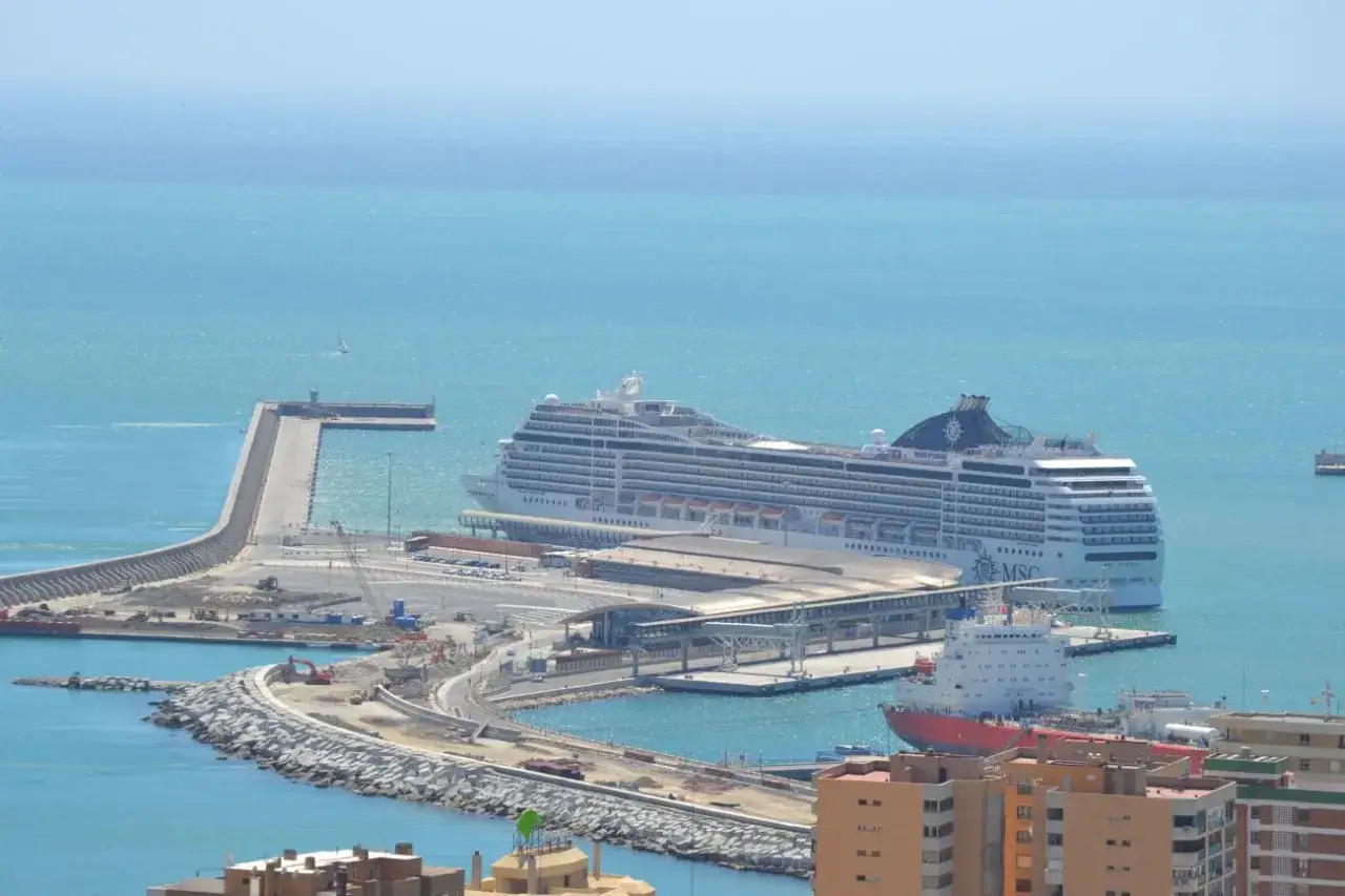 Enorme nave da crociera MSC attracca al malaga porto, con un peschereccio rosso e edifici in primo piano.