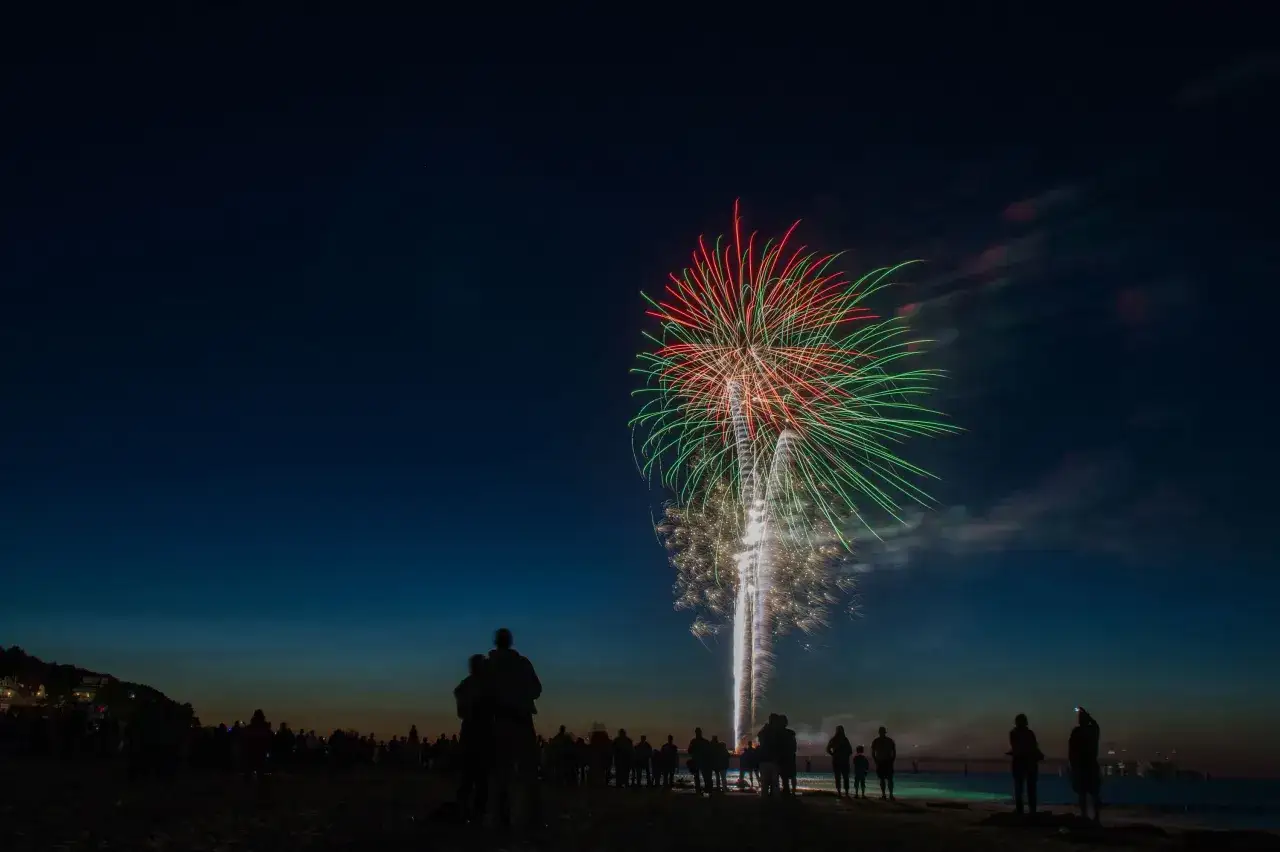 Silhouetten von Menschen am Strand beobachten ein spektakuläres Feuerwerk über dem Meer. Ein unvergesslicher Abend mit Feuerwerk Usedom.