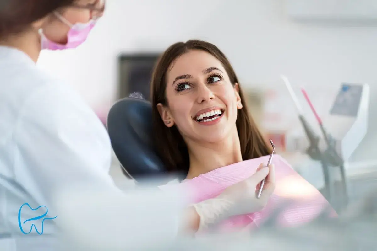 Uśmiechnięta pacjentka podczas wizyty u dentysty. Lekarz w masce przygotowuje się do badania.
