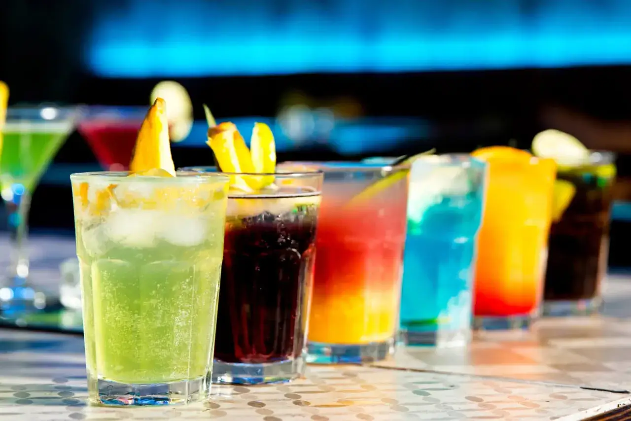 En rad färgglada drinkar, inklusive en uppfriskande tequila drink med lime och is, står redo att avnjutas.