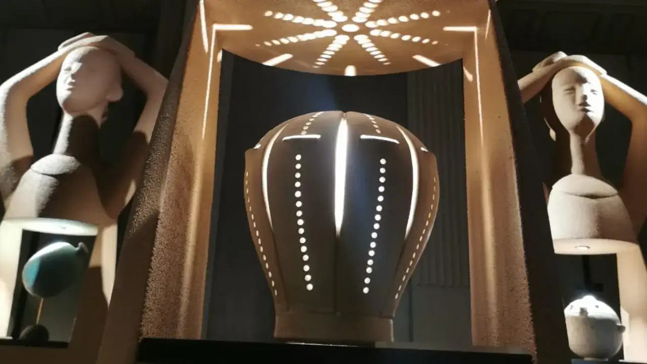 Scultura di Tonino Negri: due figure femminili stilizzate sorreggono la testa, al centro un vaso illuminato da dentro con motivi a puntini e linee.
