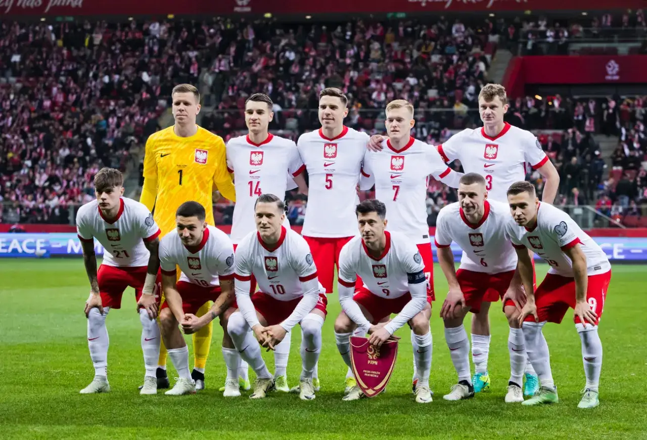 Piłkarze reprezentacji Polski w białych strojach pozują do zdjęcia na tle trybun.