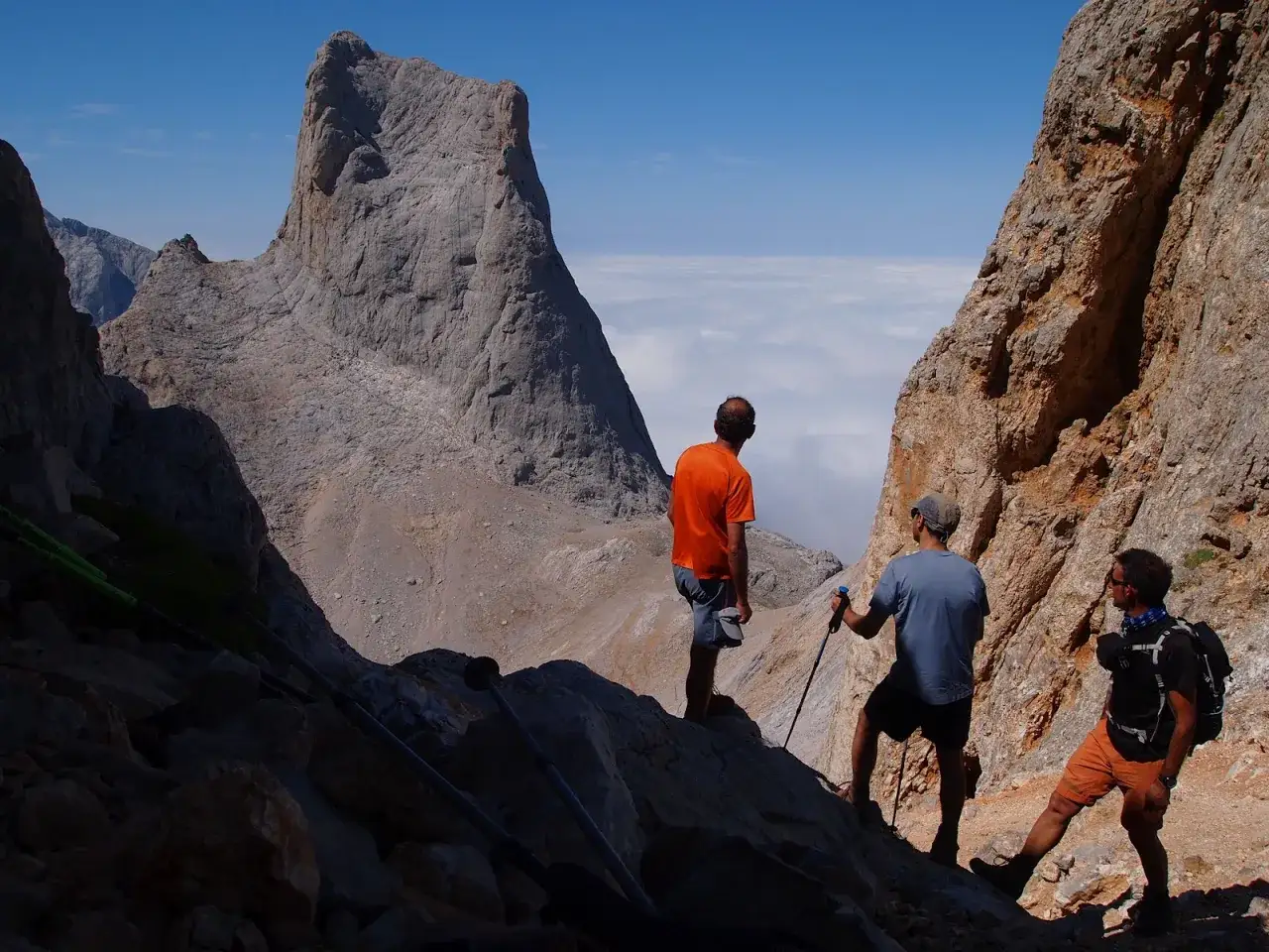Tres excursionistas contemplan el imponente Urriellu, un paisaje de roca y nubes que desafía el tiempo.