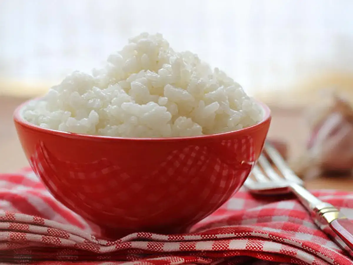 Un tazón rojo lleno de arroz blanco cocido, listo para ser disfrutado. Hay varios tipos de arroz, y este parece ser un arroz de grano corto, perfecto para acompañar cualquier comida.