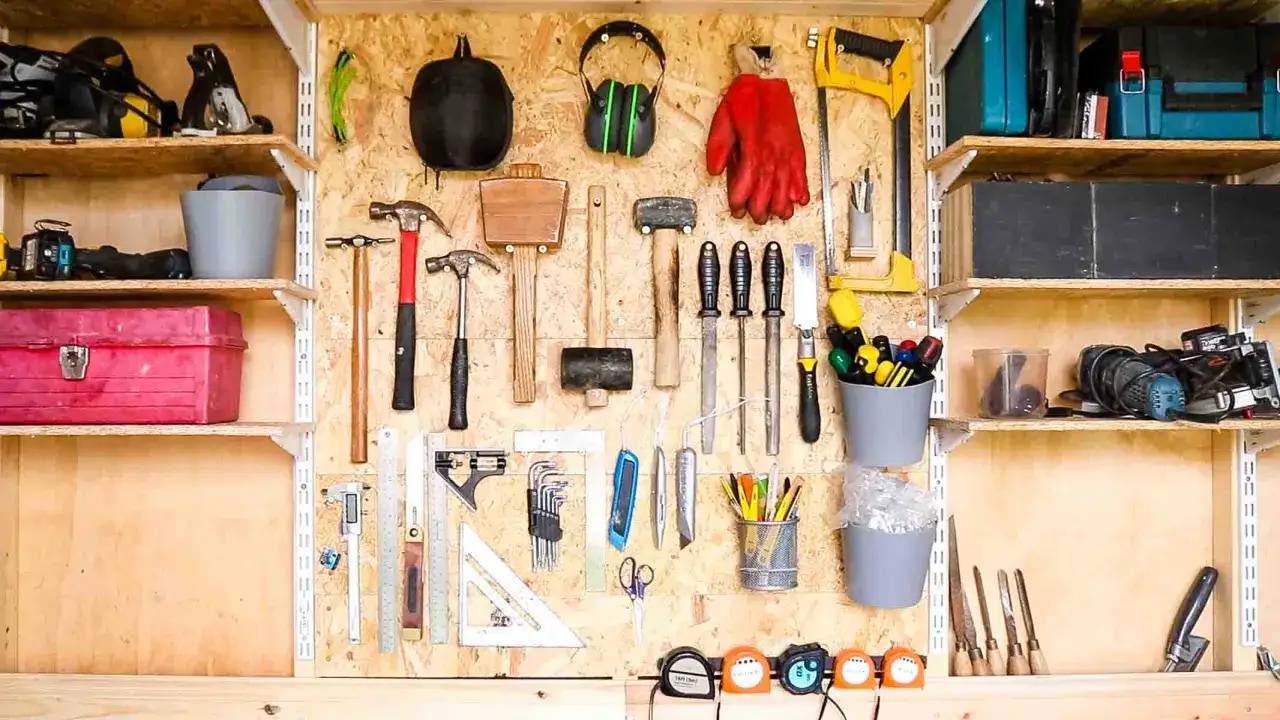 Parete porta attrezzi con pallet, martelli, guanti rossi, cuffie antirumore e altri strumenti ben organizzati.