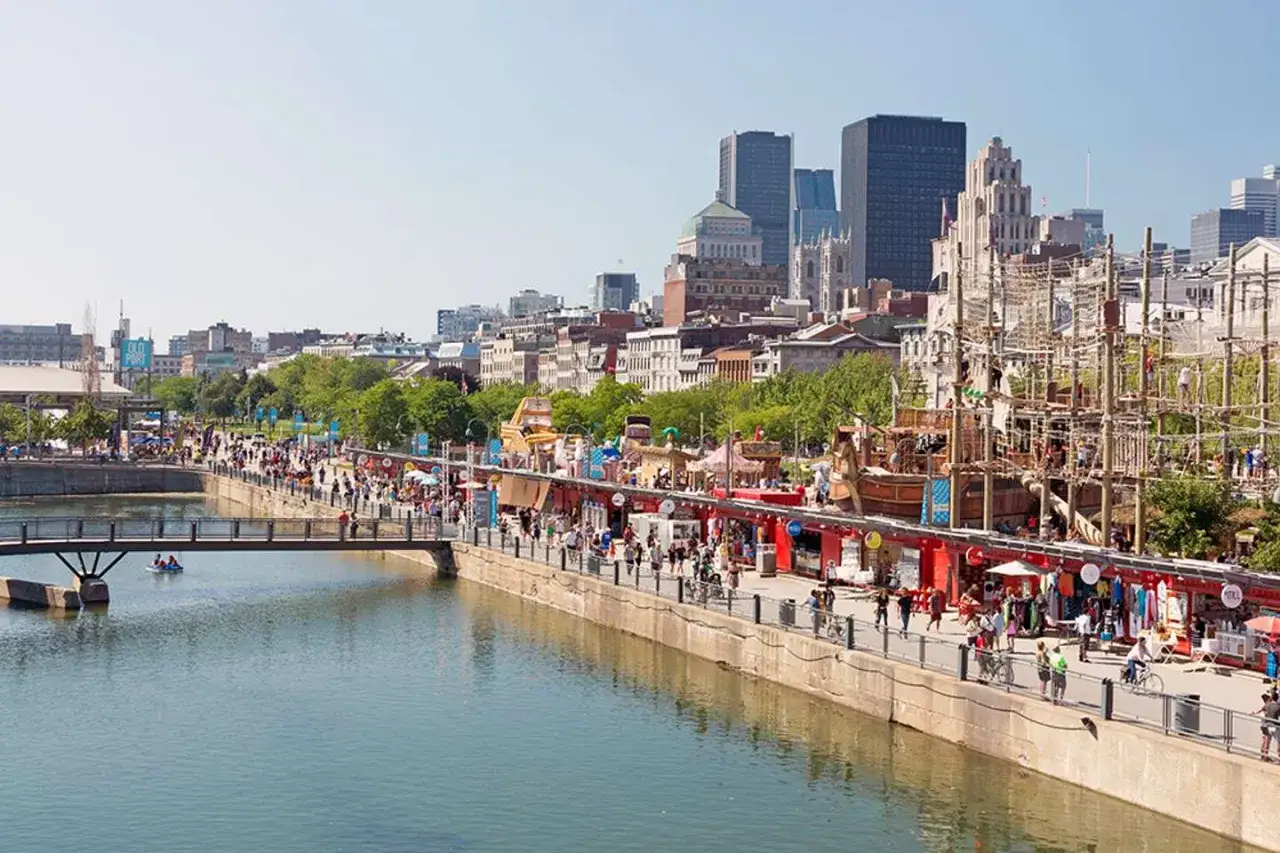 Un paseo marítimo lleno de gente en Montreal, con atracciones, tiendas y la silueta de la ciudad al fondo. ¡Mucho que ver en Montreal!