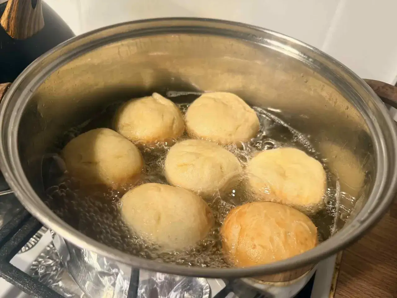 Pączki smażą się w głębokim tłuszczu, według starego przepisu na pączki. Widać, jak bąbelki otaczają złociste ciasto.