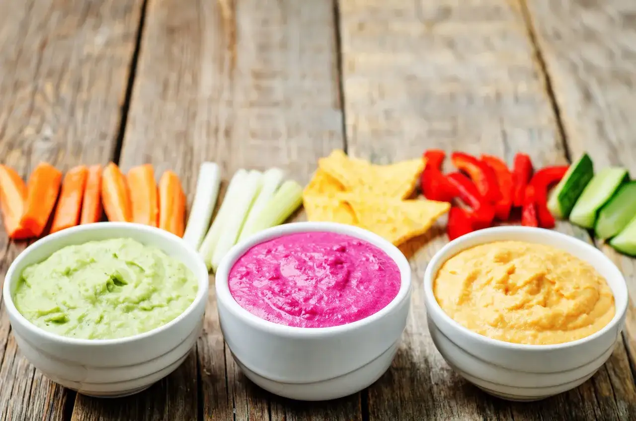 Trois bols de trempettes color&eacute;es (vert, rose, jaune) avec des crudit&eacute;s et des chips. Un encas healthy parfait pour un ap&eacute;ritif.