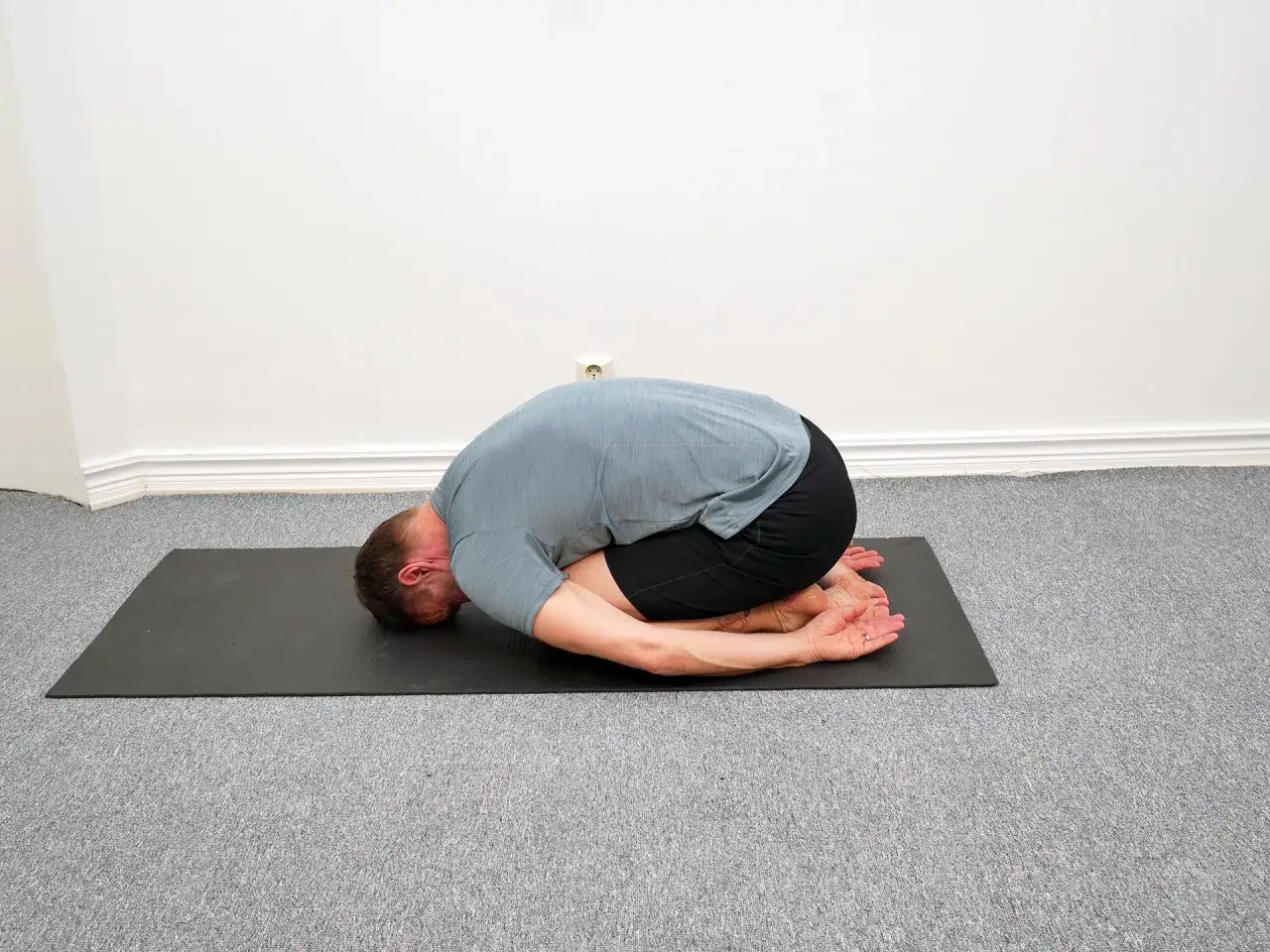 Man i barnställning på yogamatta, en lugnande position för fascia yoga.