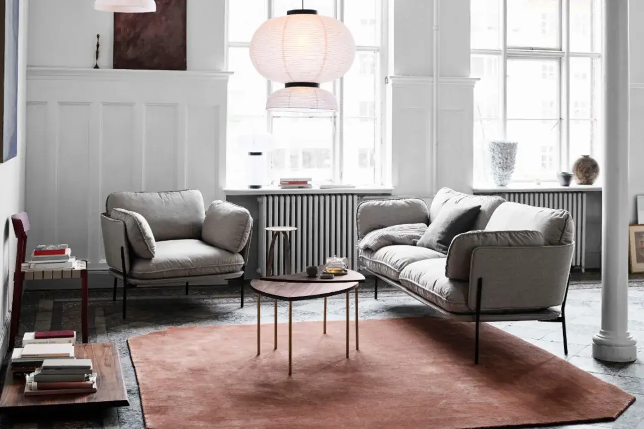Ein gemütliches Wohnzimmer mit einem grauen Sofa, das von einem warmen, rosenroten Teppich umgeben ist.