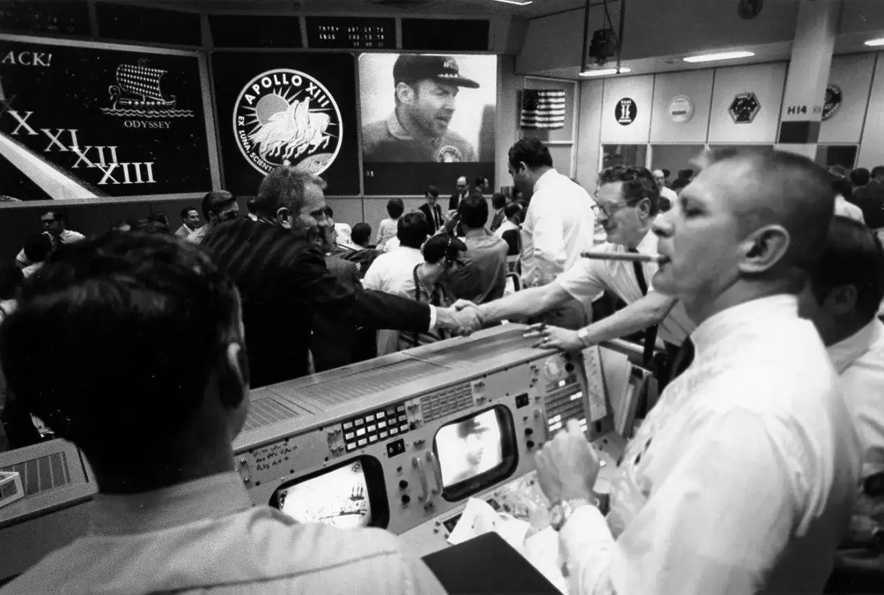 Uścisk dłoni w centrum kontroli misji Apollo 13. Na ekranie widać astronautę.