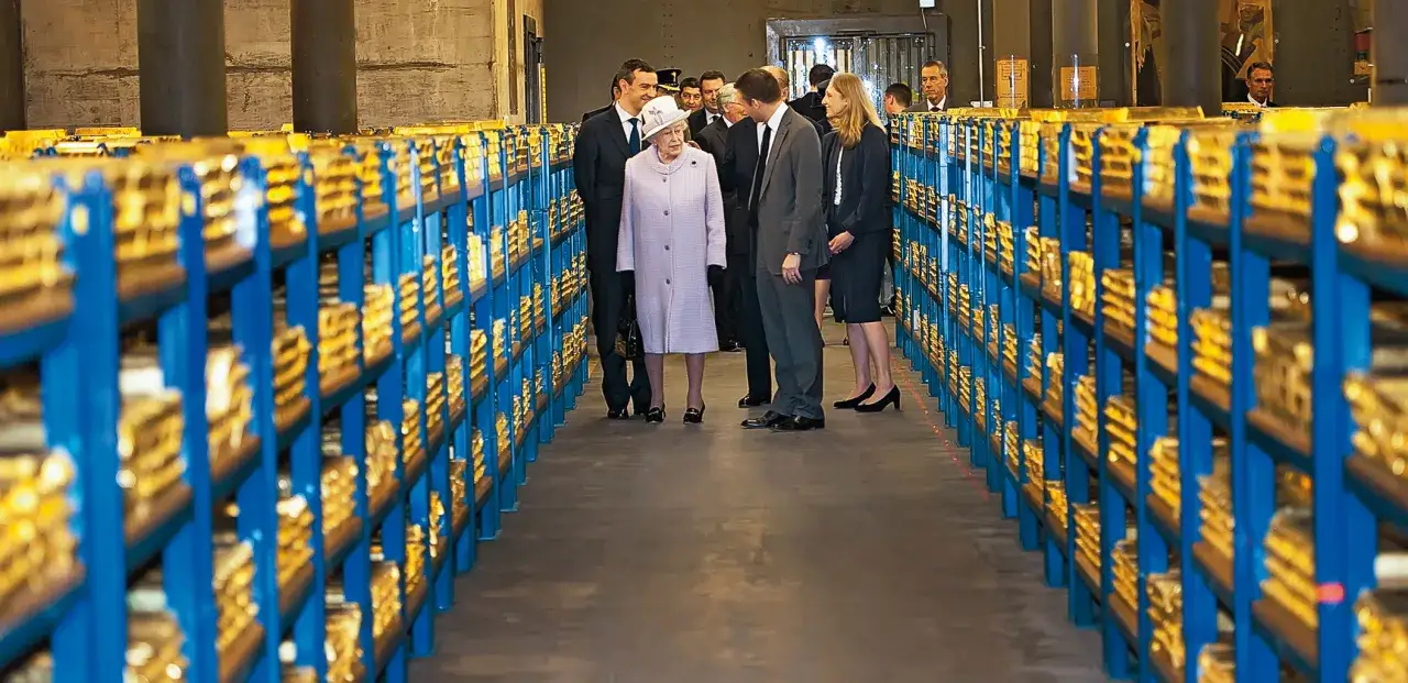 Królowa Elżbieta II w magazynie pełnym sztabek złota, przypominającym zasoby NBP.