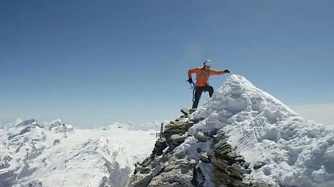 Alpinista en la cima nevada, alcanzando un nuevo r&eacute;cord en el Cervino. El cielo azul y las monta&ntilde;as heladas lo rodean.