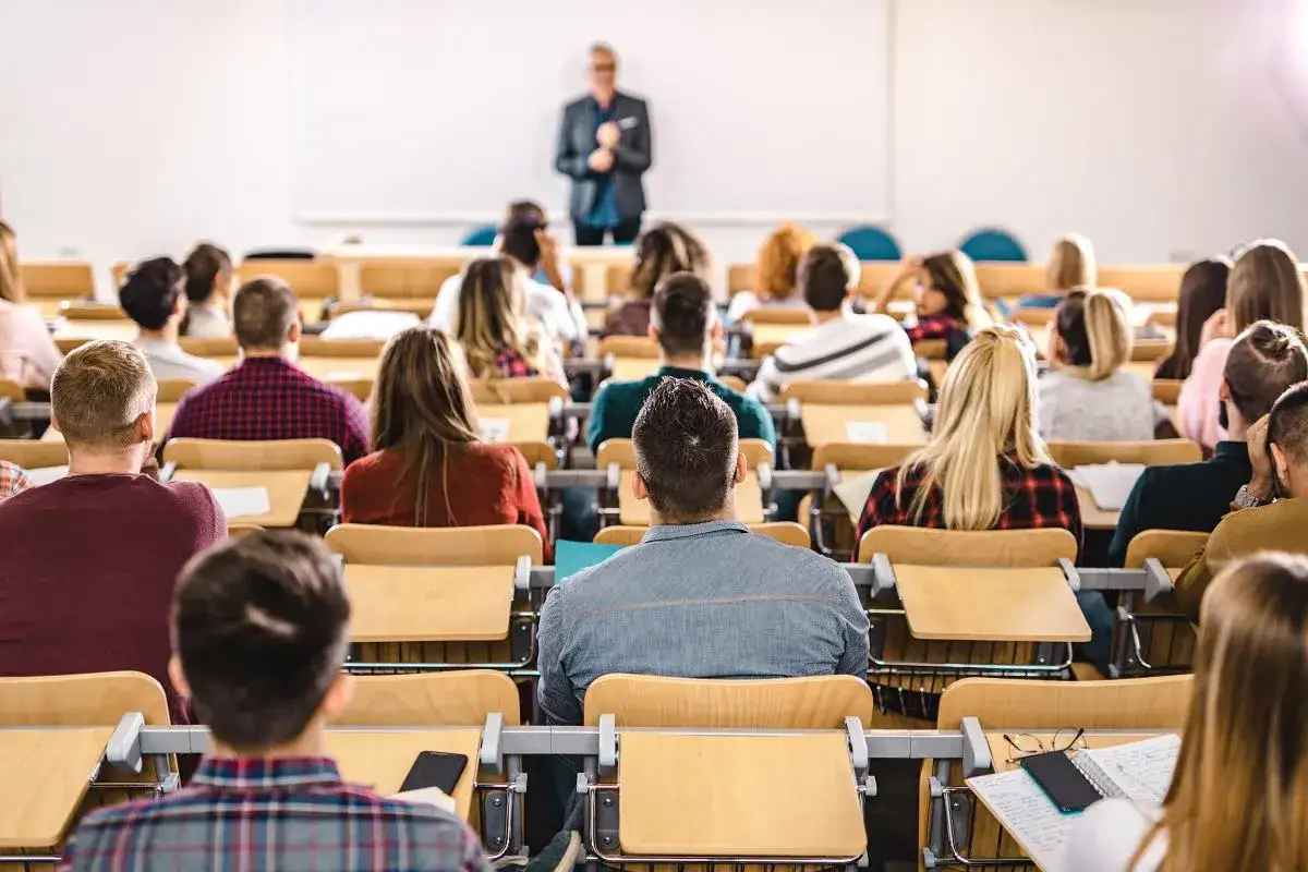 Wykład na uczelni, studenci siedzą w ławkach. Ciekawe, ile zarabia profesor na uczelni, że może prowadzić takie zajęcia.