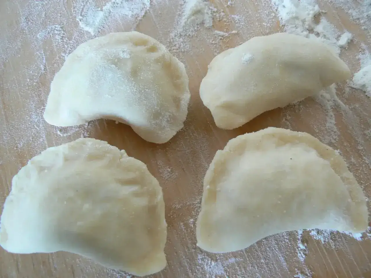 Surowe pierogi na drewnianej desce, posypane mąką. Idealne na przepis na ciasto na pierogi Magdy Gessler.