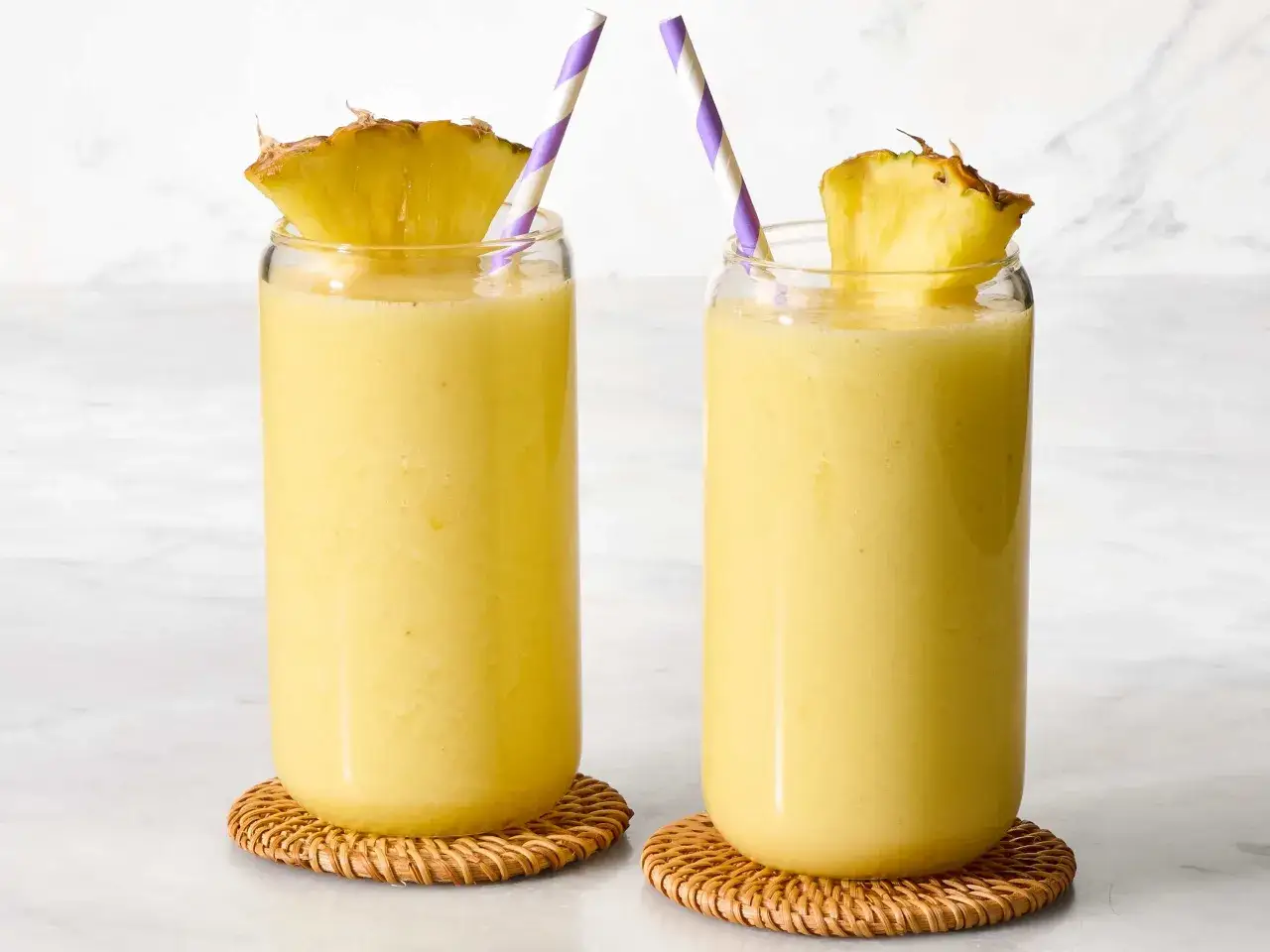 Dwa orzeźwiające smoothie z ananasem, udekorowane plasterkami owocu i kolorowymi słomkami, gotowe do wypicia.