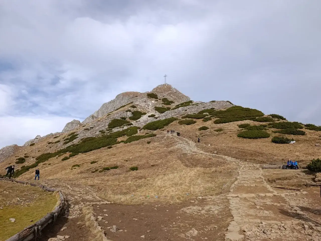 Kamienista ścieżka prowadzi na szczyt Giewontu, gdzie widnieje krzyż. Czy Giewont jest trudny? Turyści idą w g&oacute;rę, pokonując skaliste zbocza.