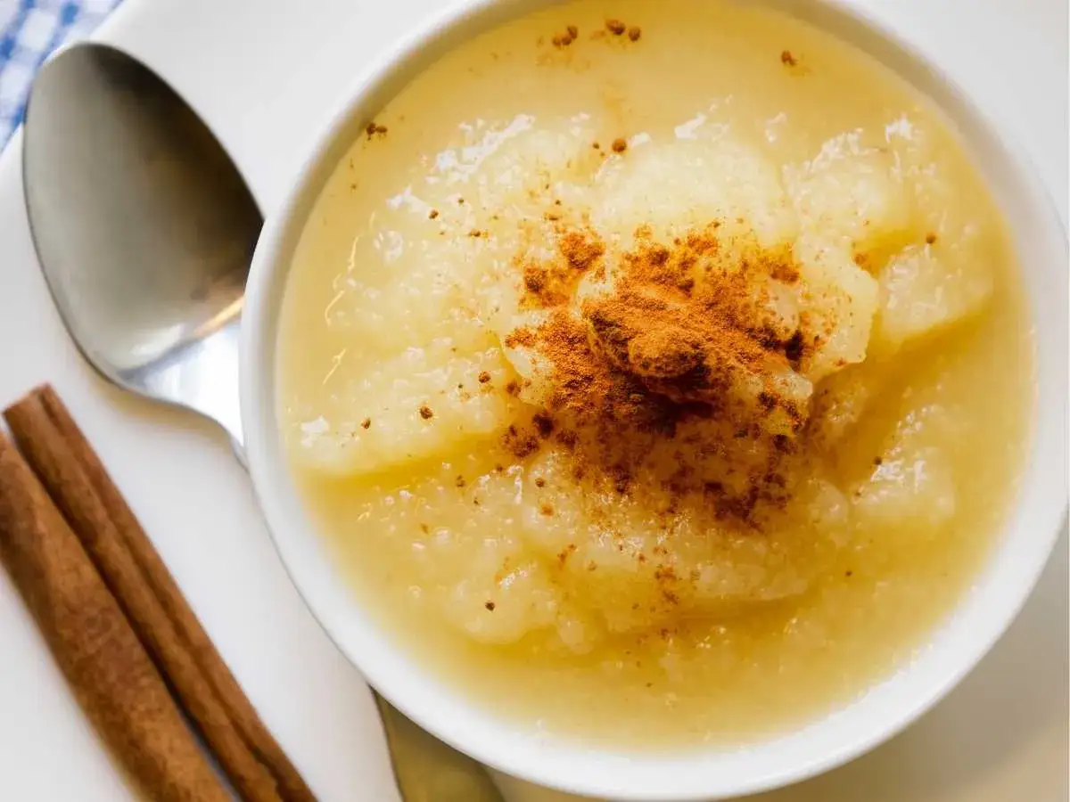 Deliciosa compota de manzana casera, espolvoreada con canela y servida con una cuchara y dos ramas de canela.