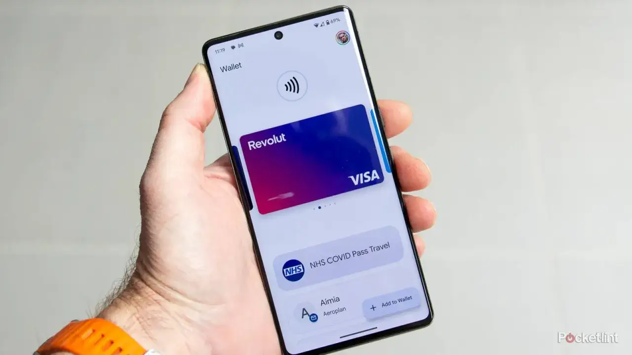 Dłoń trzyma smartfon z otwartą aplikacją Portfel Google, wyświetlającą kartę Revolut i NHS COVID Pass. Czy portfel Google jest bezpieczny? Tak, zapewnia ochronę danych.