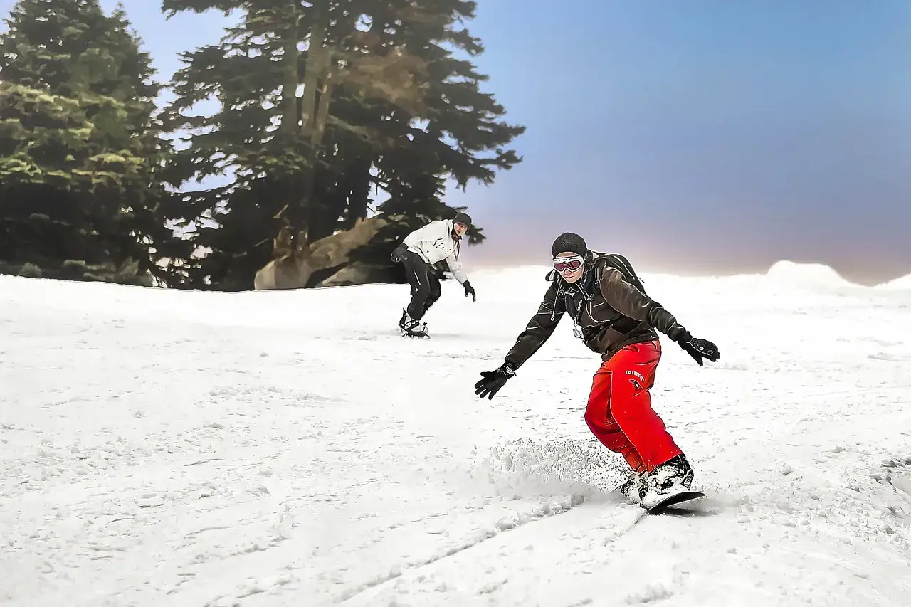 Dwóch snowboardzistów zjeżdża po ośnieżonym stoku. Zastanawiasz się, jak dobrać snowboard? Wybierz odpowiedni sprzęt i ciesz się jazdą!