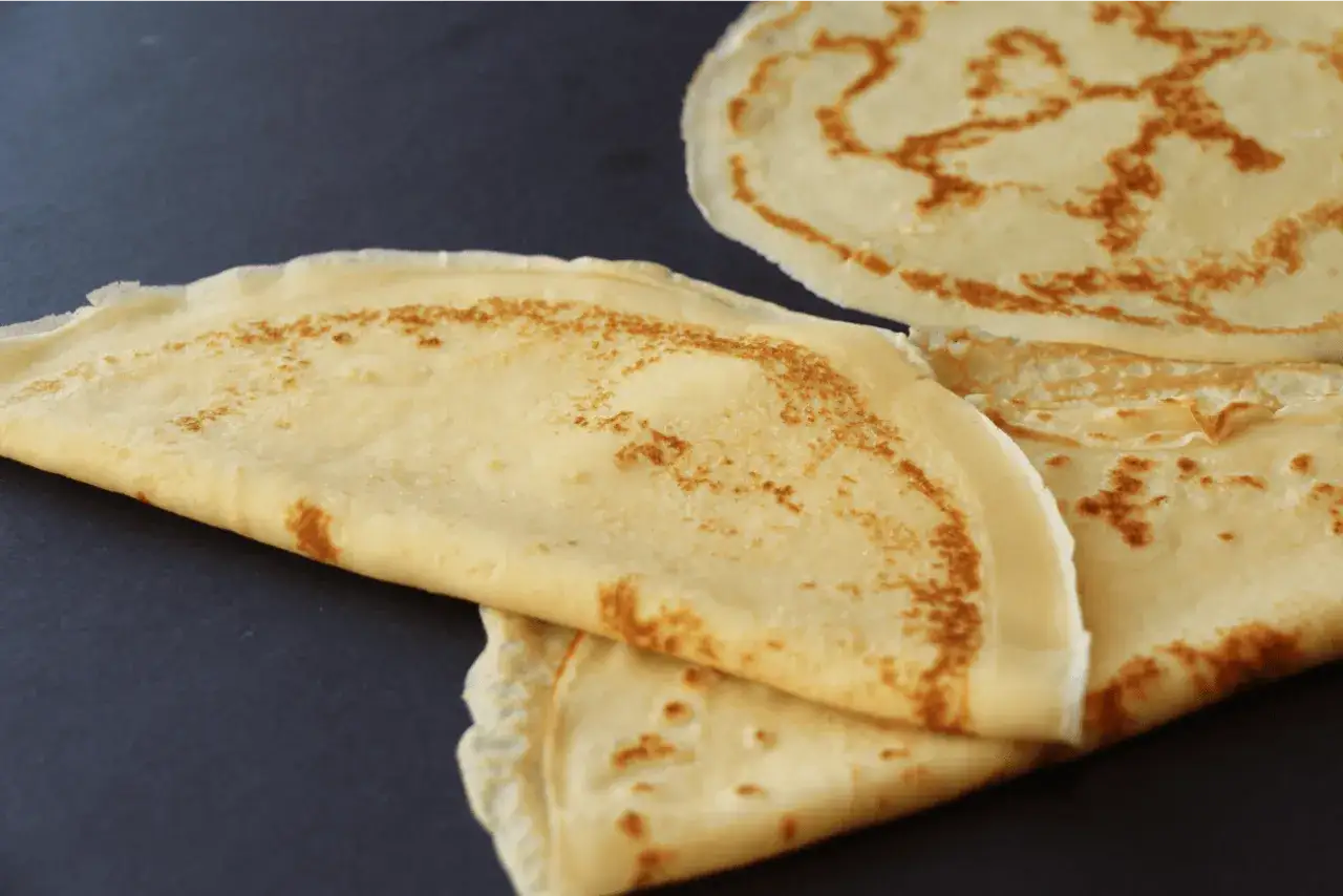 Crêpes dorées, parfaites pour une recette crêpe 2 œufs. Elles sont empilées sur un fond sombre, prêtes à être garnies.