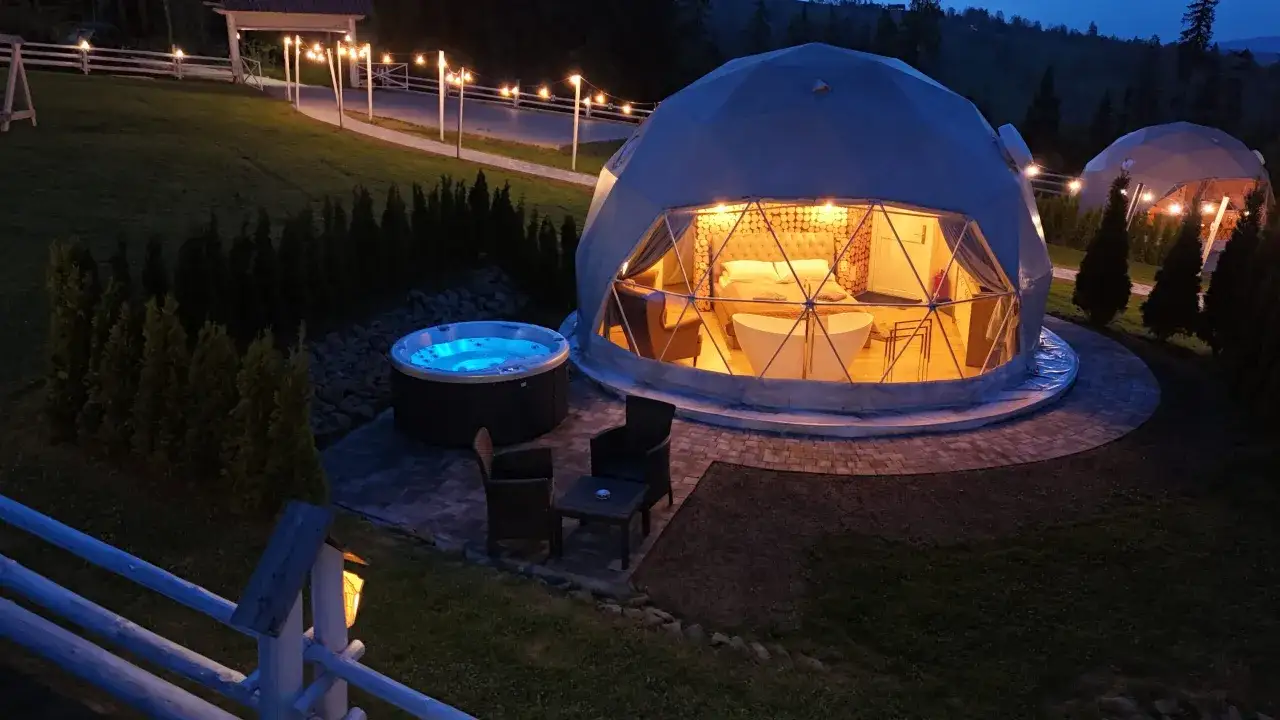 Nocne, luksusowe glamping w Polsce. Kopuła z łóżkiem i wanną, obok jacuzzi i meble ogrodowe.