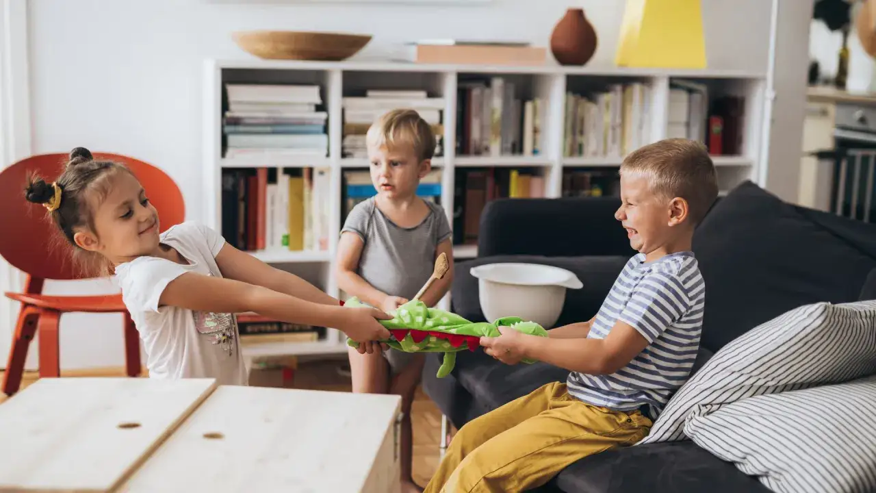 Drei Kinder streiten sich aggressiv um ein Stofftier. Geschwister-Eifersucht und Aggression sind in diesem Moment deutlich zu sehen.
