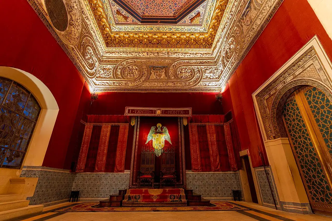 Sala de los Reyes del Alcázar de Segovia, con dos tronos, un escudo real y un techo ricamente decorado.