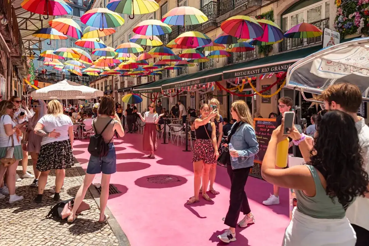 Ombrelli colorati illuminano una strada di Lisbona, con gente che scatta foto e gode dell'atmosfera vivace.