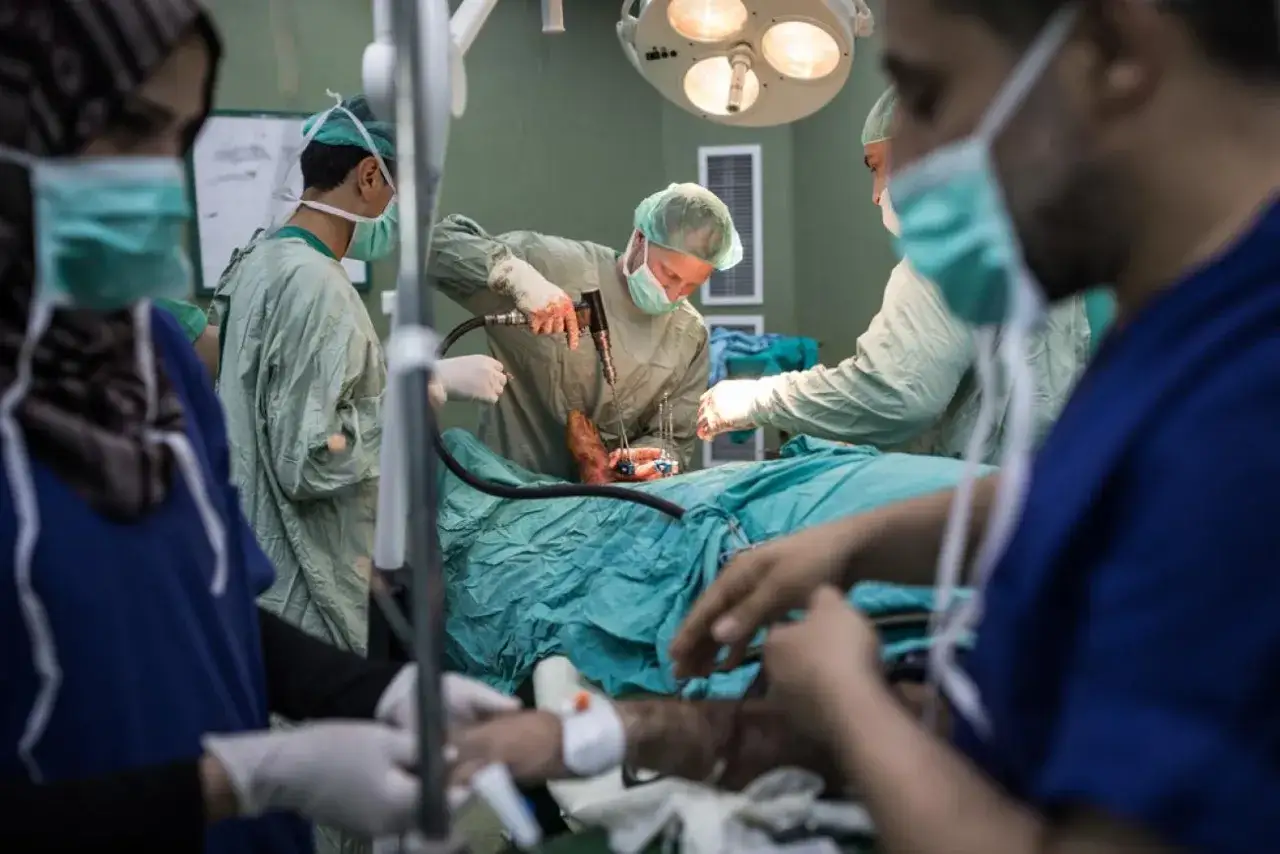 Une équipe médicale, dont un médecin spécialiste, opère un pied. Ils utilisent des instruments chirurgicaux sous un éclairage intense.
