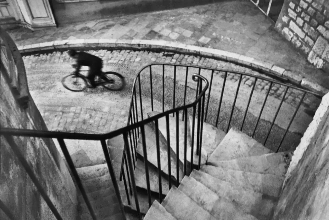 Ein Radfahrer rast über Kopfsteinpflaster, eingefangen in einem Moment der Bewegung, wie in den berühmten henri cartier-bresson fotos.