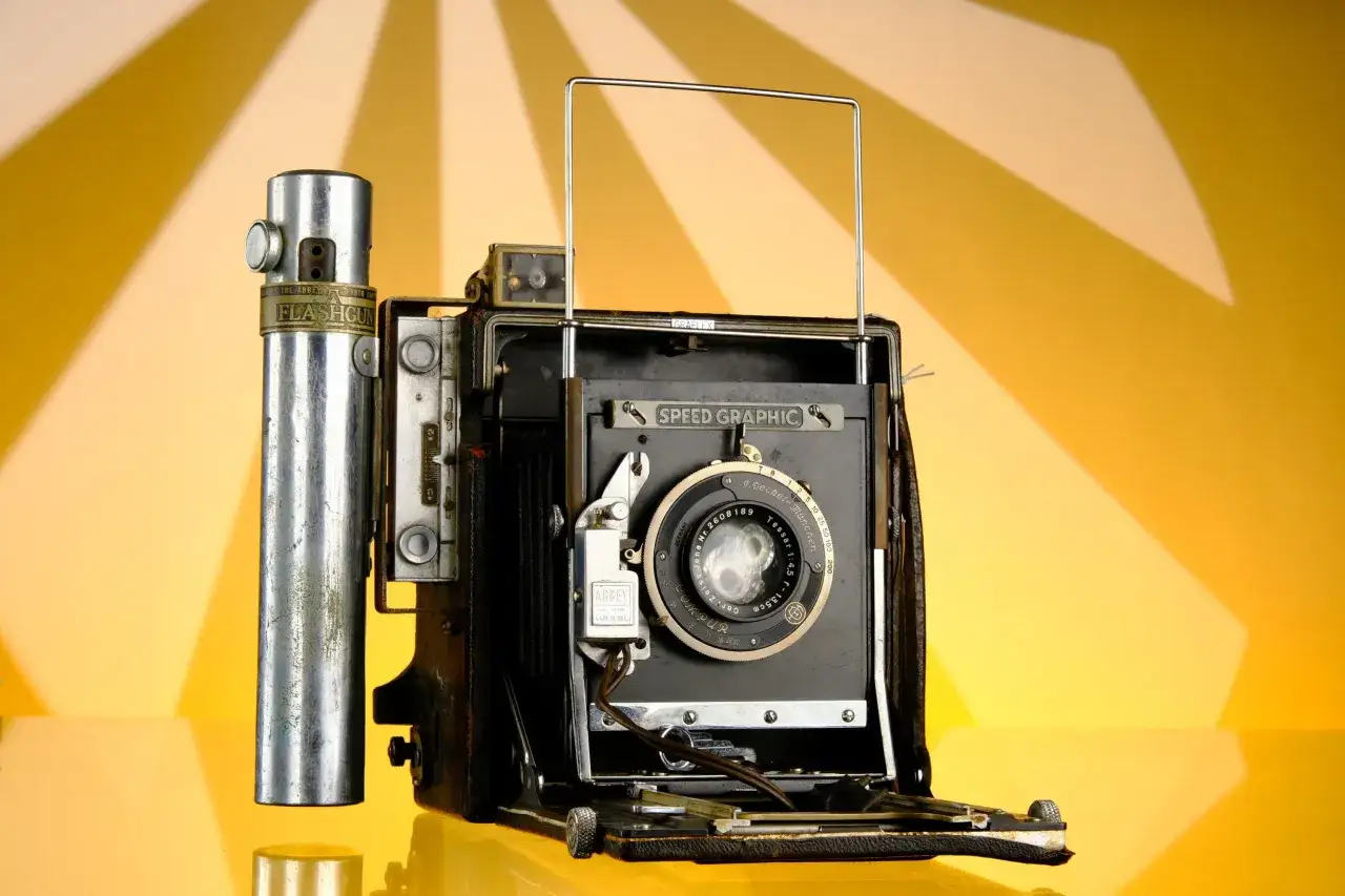 A vintage Graflex Speed Graphic camera with a flashgun attachment, ready to capture history.
