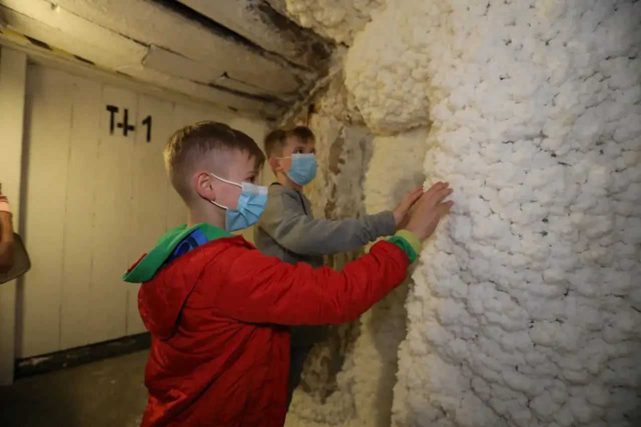 Dzieci w maskach dotykają białych, chropowatych formacji solnych podczas zwiedzania trasy turystycznej Wieliczka.