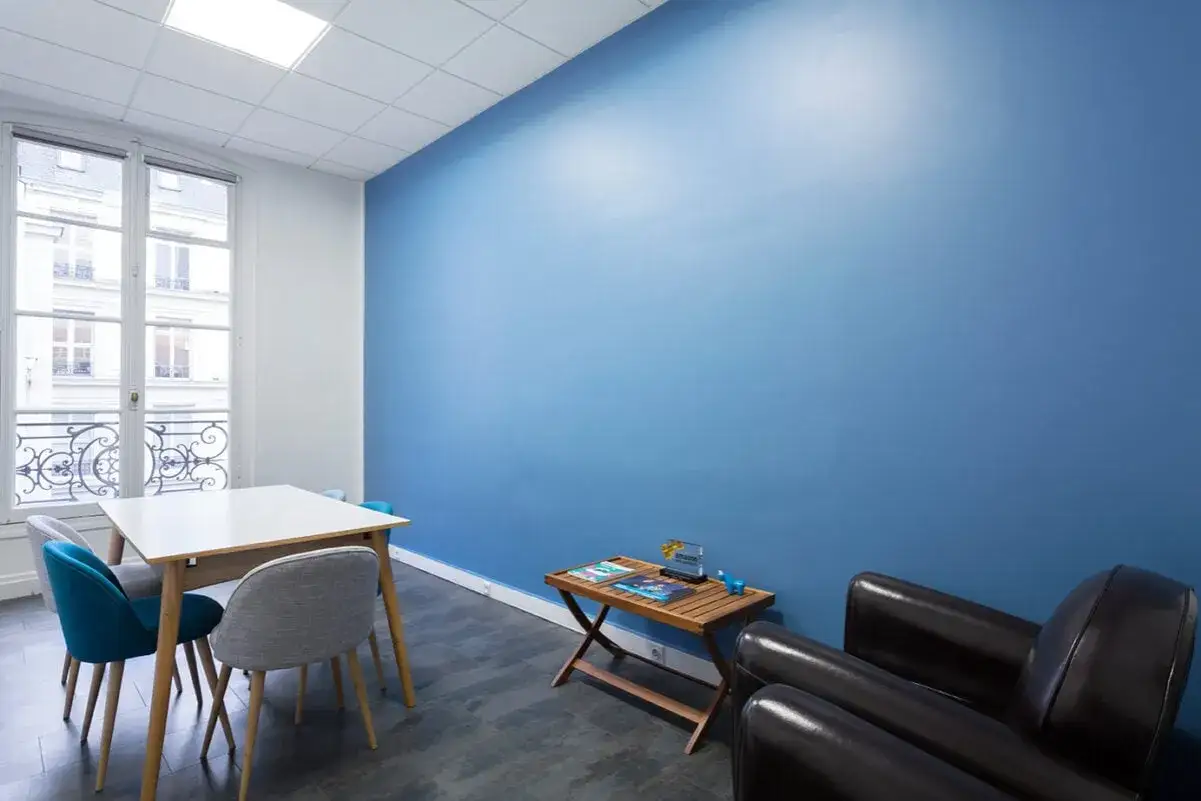 Un salon moderne avec une grande murale bleu vif, finition peinture mat ou satin, une table et des fauteuils confortables.