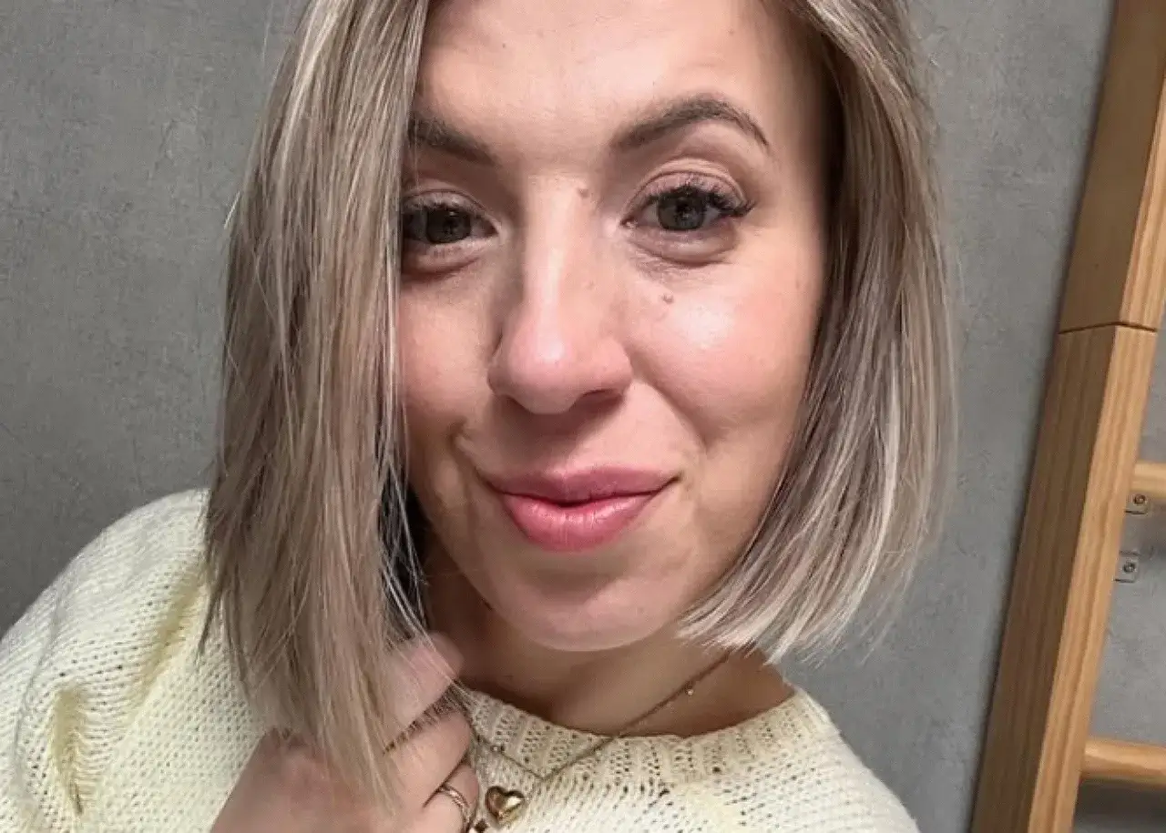 Uśmiechnięta Małgorzata, która szuka żony, w jasnym swetrze i z serduszkiem na szyi.