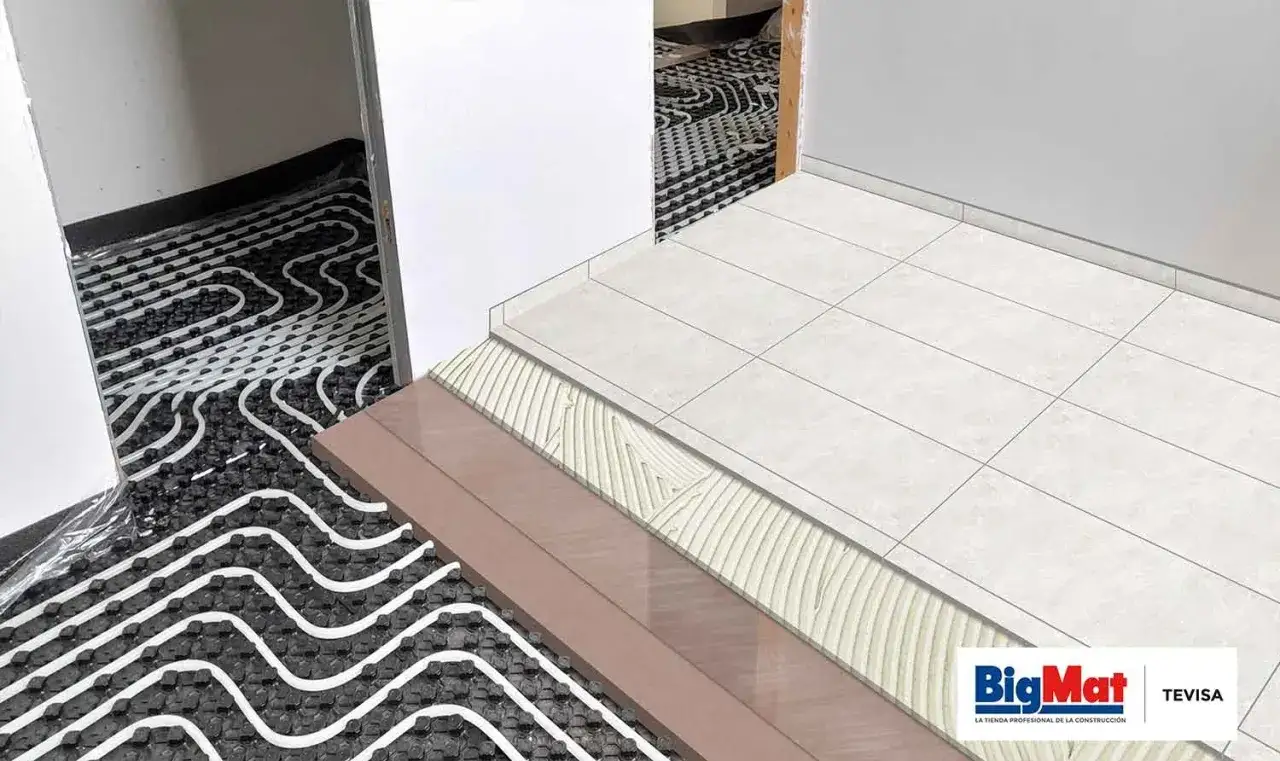 Instalaci&oacute;n de suelo radiante con tuber&iacute;as en zigzag sobre aislante negro. Capas de mortero y baldosas blancas completan el sistema.